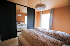 A bedroom with a bed, a large mirror, and a hanging light fixture. - Light, Calm and Modern Corner Apartment (Argir)