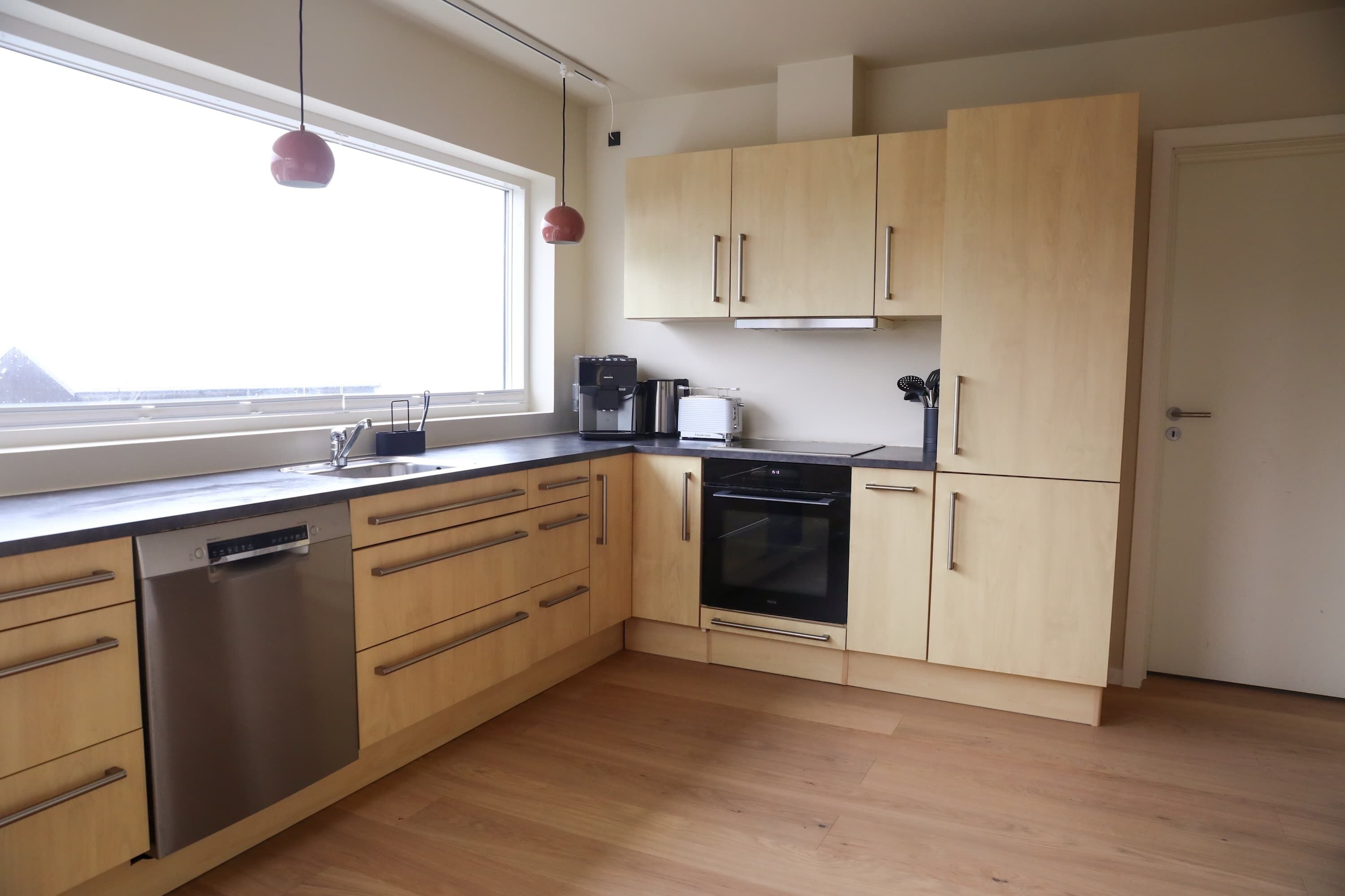 Eine moderne Küche mit Holzausstattung, einem Geschirrspüler, einer Kaffeemaschine und einem Toaster.