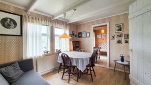 A dining area with a table and chairs, a sofa, a radiator, and a bookshelf.