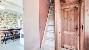 A staircase with a wooden handrail leading to a door, a dining area with chairs and a table, and a wall with a patterned wallpaper.