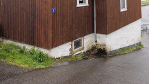 Un edificio de madera con techo verde, una ventana pequeña y un cartel con el número 2 al costado.