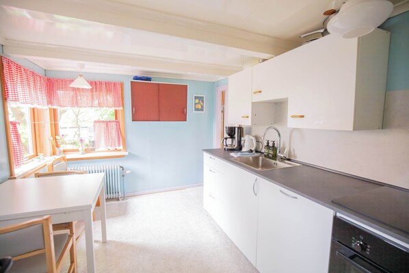 A kitchen with a white countertop, a sink, and a window with red curtains.