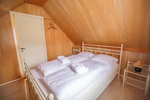 A single bed with white linens in a room with wooden walls and a sloped ceiling.