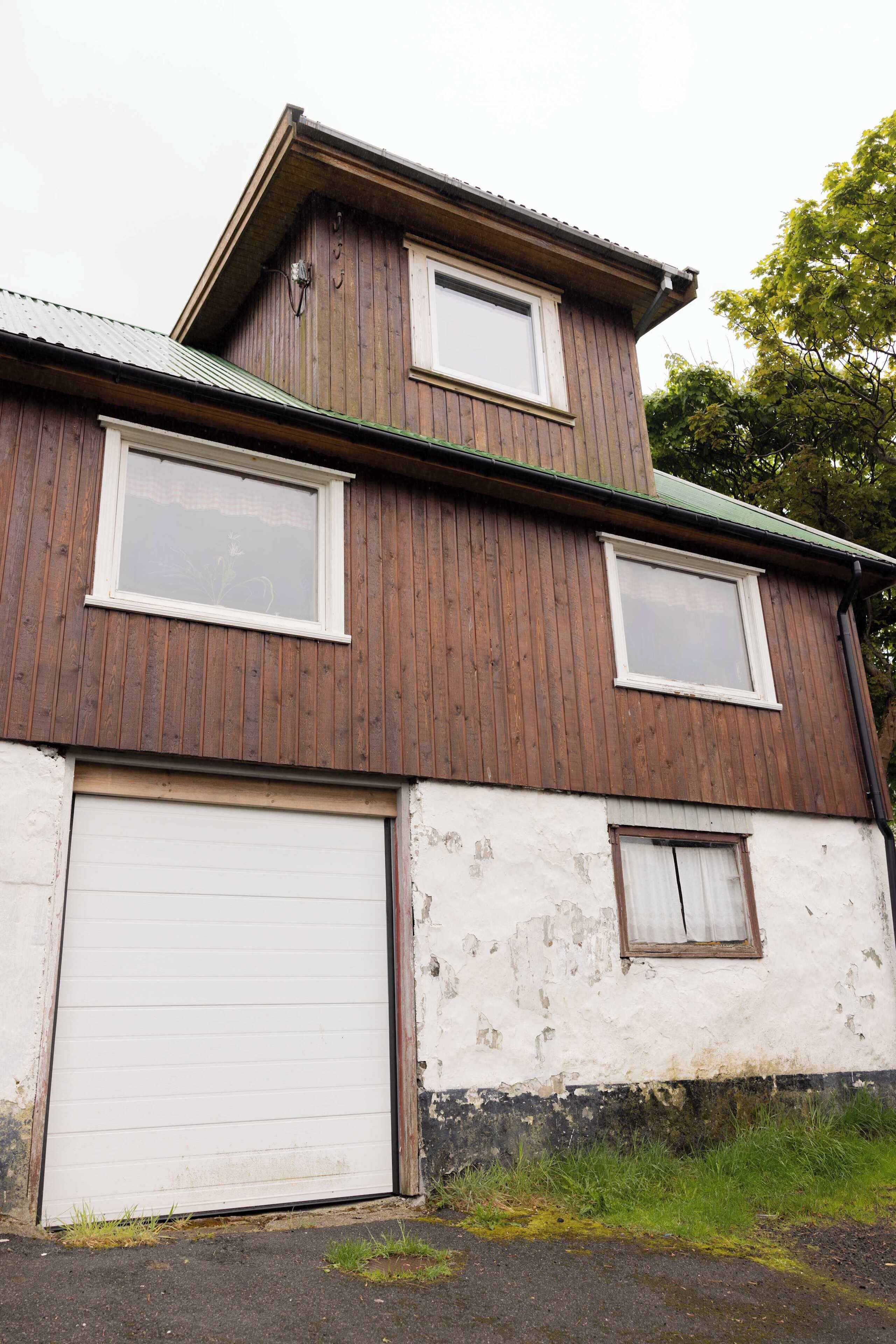 Un bâtiment à deux étages, doté d’une porte de garage et de deux fenêtres à l’étage supérieur.