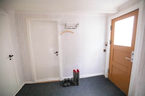A hallway with a white door, a wooden door, and a shoe rack with shoes.