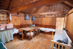 A rustic wooden interior with a dining table, chairs, a bench, and a kitchen area. - Historic Turf-Roofed House (Tjørnuvík)