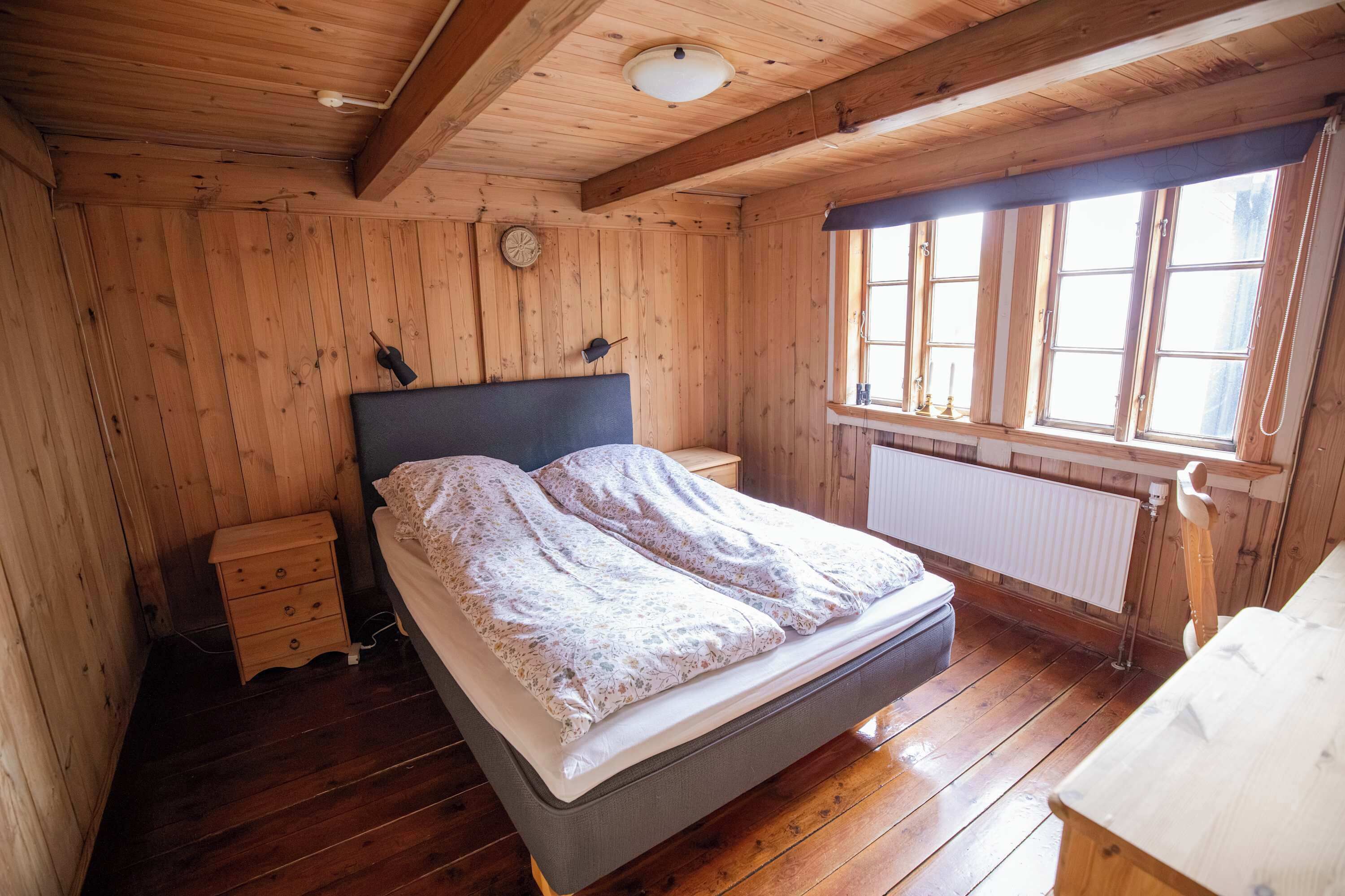 Een slaapkamer met houten lambrisering, een bed, nachtkastjes, een raam en een radiator.