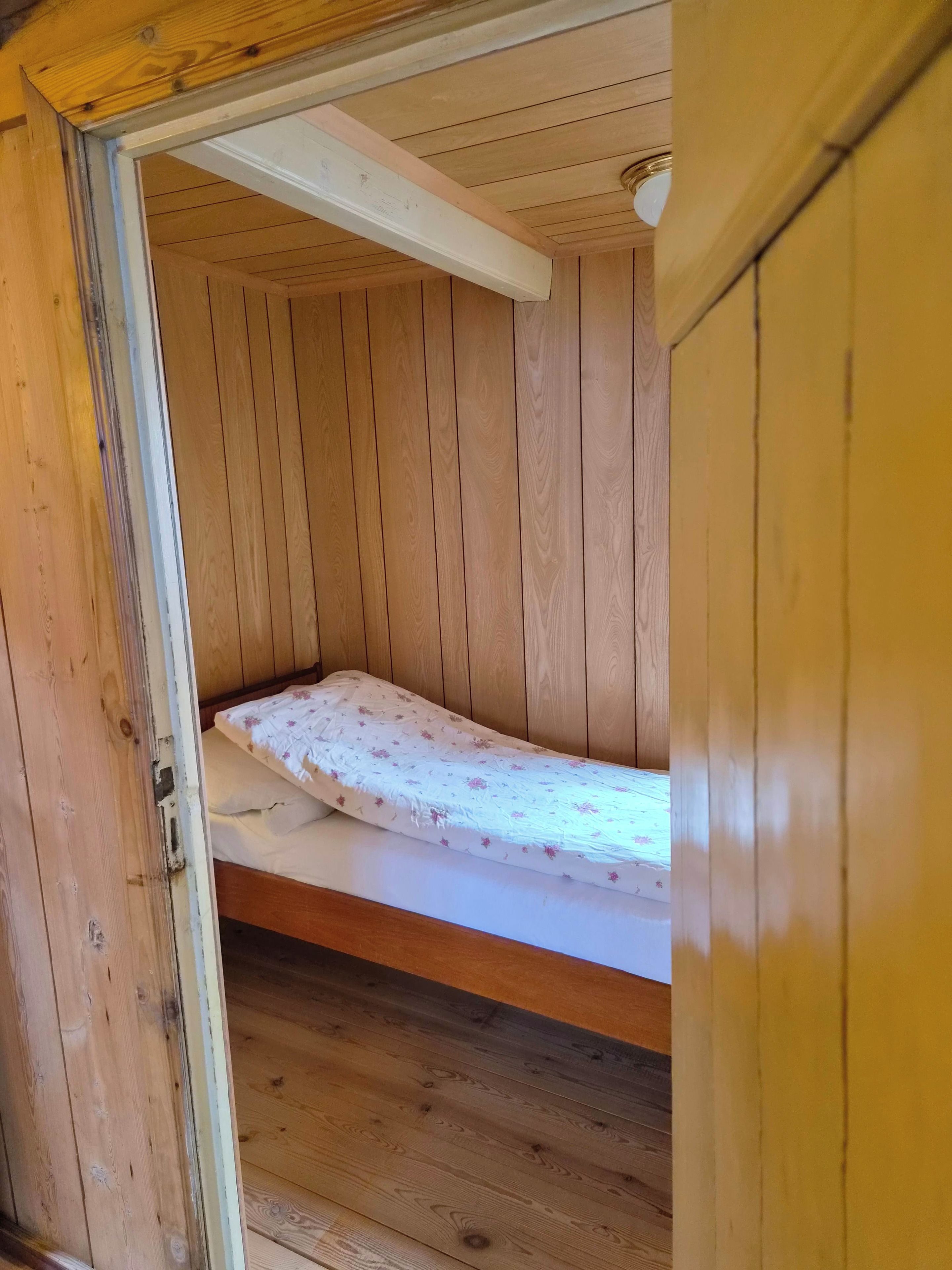 A wooden room with a single bed, a door, and a ceiling light fixture.