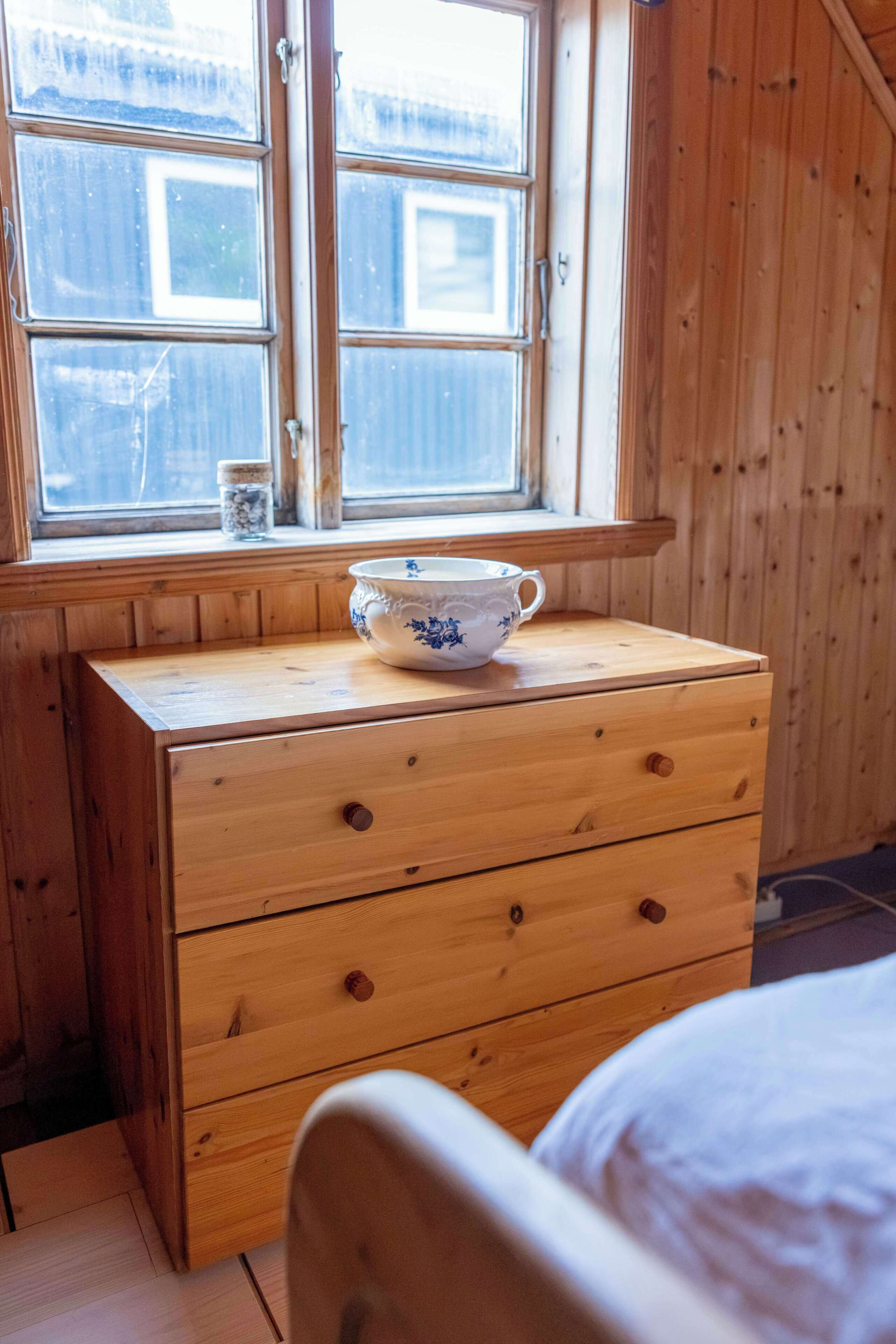 Un comò di legno con cassetti, una finestra che si affaccia su un paesaggio innevato e una ciotola sul comò.