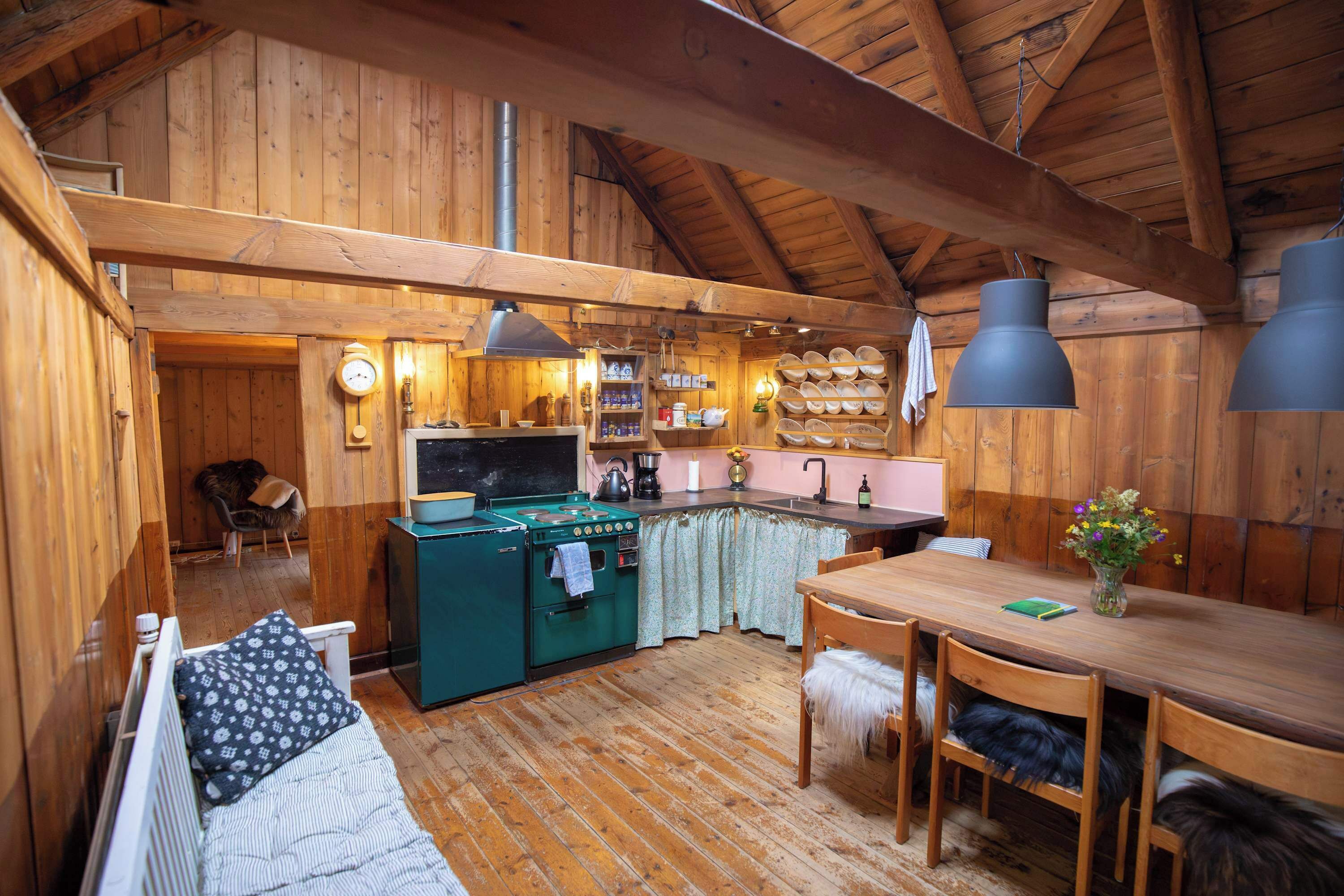 A cozy cabin interior with a wooden dining area, a kitchen with a stove, and a living space with a sofa.
