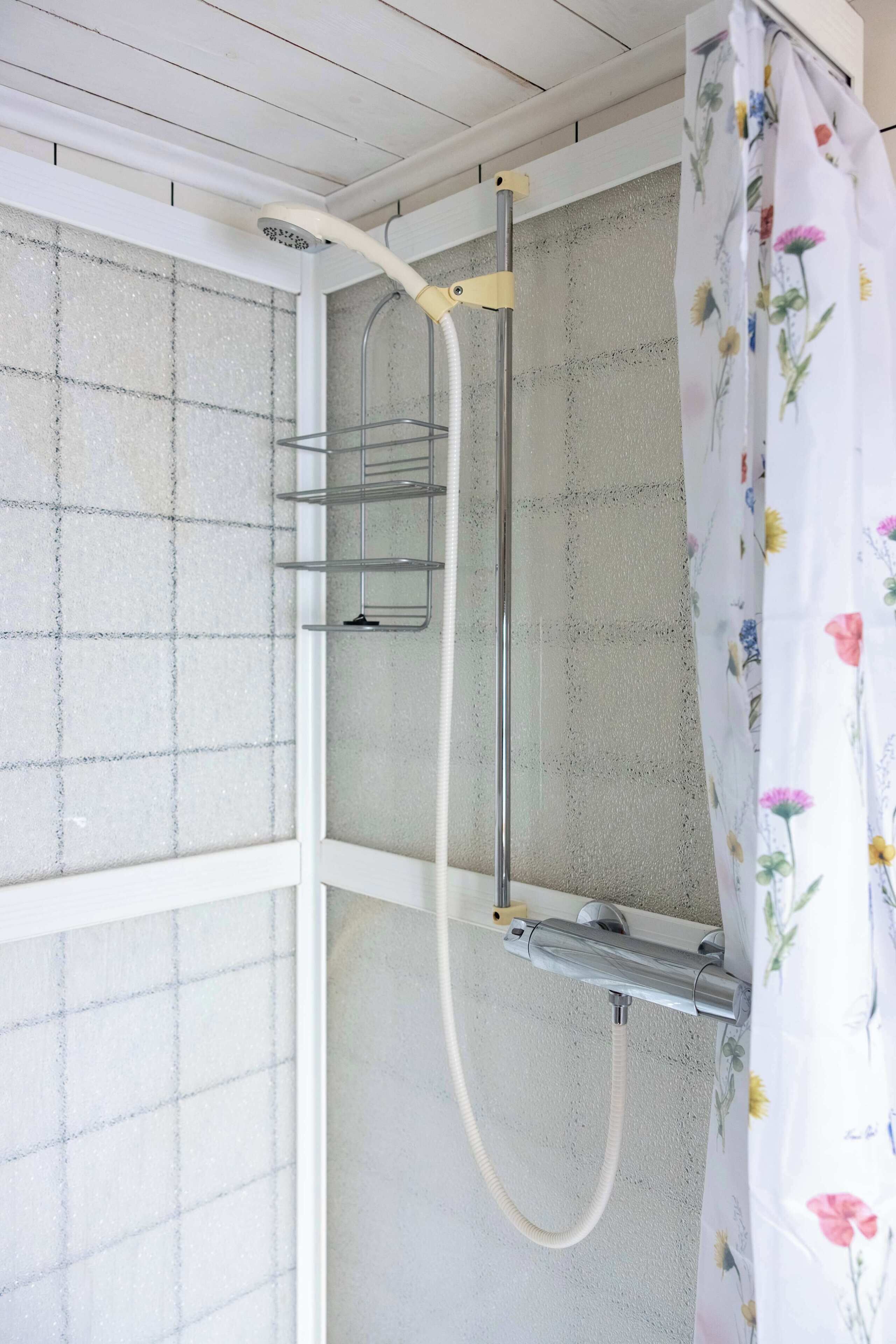 A shower area with a showerhead, a hose, and a metal shelf.