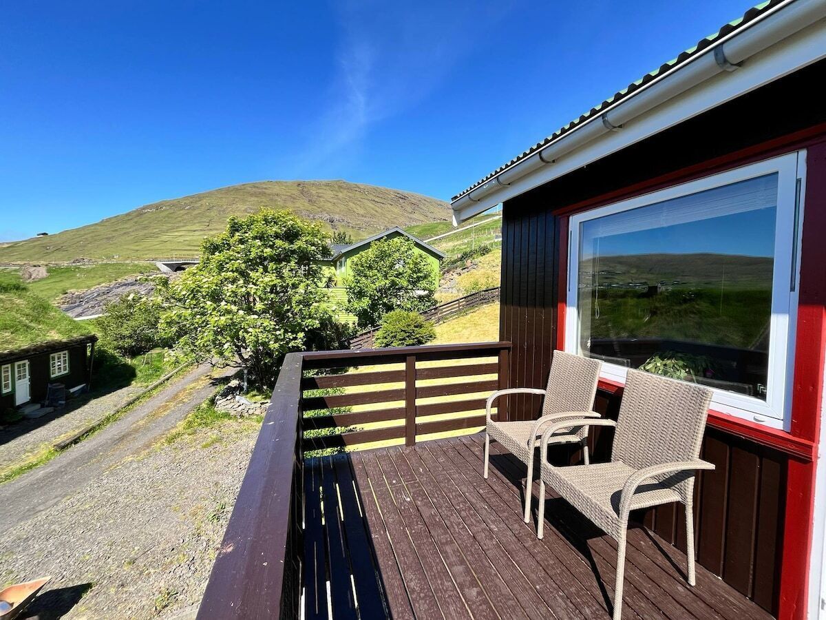 A wooden deck with two wicker chairs and a large window overlooking a hilly landscape.