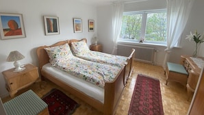 A bedroom with a double bed, two bedside tables, a window with curtains, and a radiator.