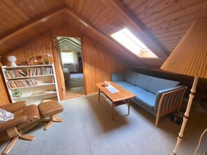 A cozy room with a wooden ceiling, a sofa, a coffee table, a bookshelf, and a lamp. - 5BR Charming Villa with Stunning Views - 9 guests (Vestmanna)