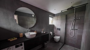 Un bagno moderno con uno specchio rotondo, un lavandino, un water e una cabina doccia.