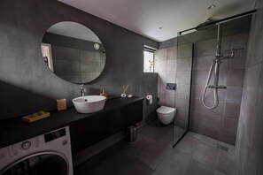 Een moderne badkamer met een ronde spiegel, een wastafel, een toilet en een inloopdouche.