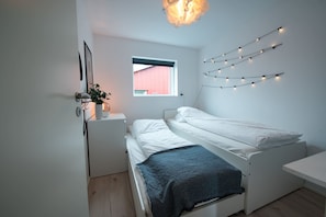 Un dormitorio minimalista con una cama individual, una mesita de noche pequeña, una ventana y luces colgantes en la pared.