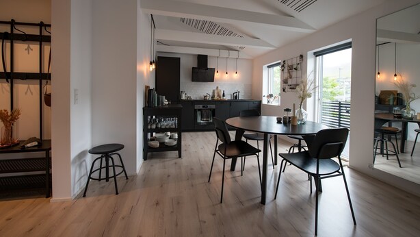 Una cucina moderna con zona pranzo, caratterizzata da una grande finestra, mobili in legno nero e pavimento in legno.