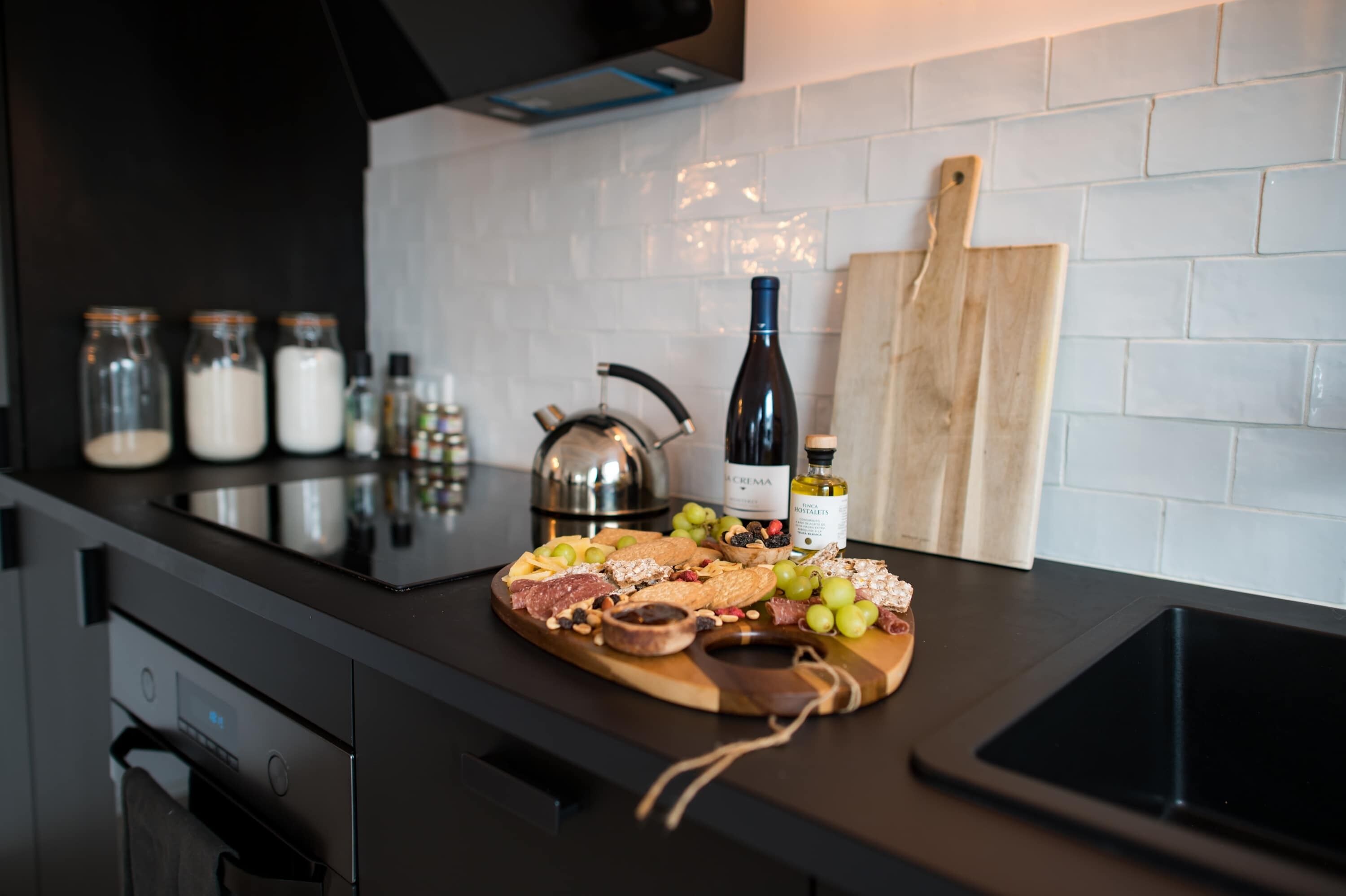A kitchen counter with a charcuterie board, jars, a wine bottle, and a cutting board.