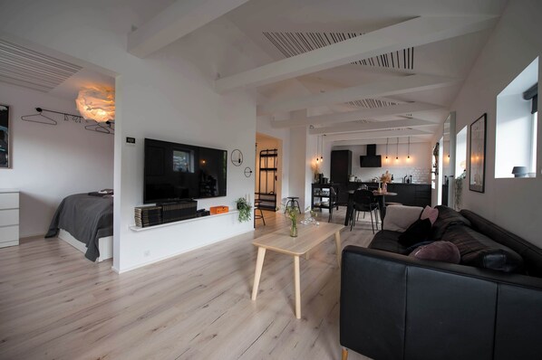 Una sala moderna con un televisor de pantalla plana, un sofá, un comedor y una cocina al fondo.