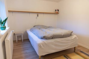 Une chambre à coucher avec un lit, une petite table de chevet, un radiateur, une plante en pot et une étagère avec un jouet.