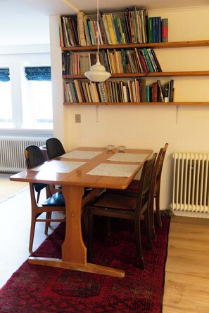 A room with a wooden table, chairs, a red patterned rug, and a bookshelf filled with books. - Cozy Apartment in a Quiet Area of Torshavn (Tórshavn)