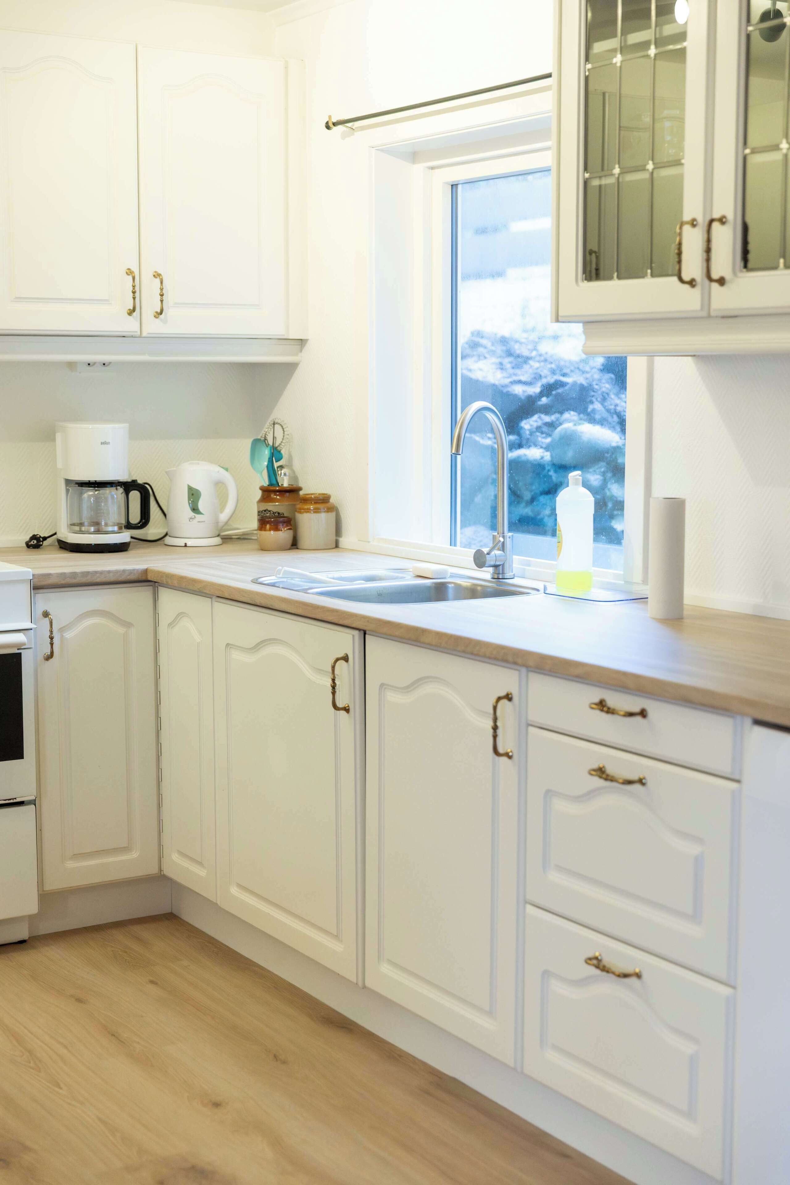 A kitchen with white cabinetry, a coffee maker, a kettle, and a window with a view of trees.