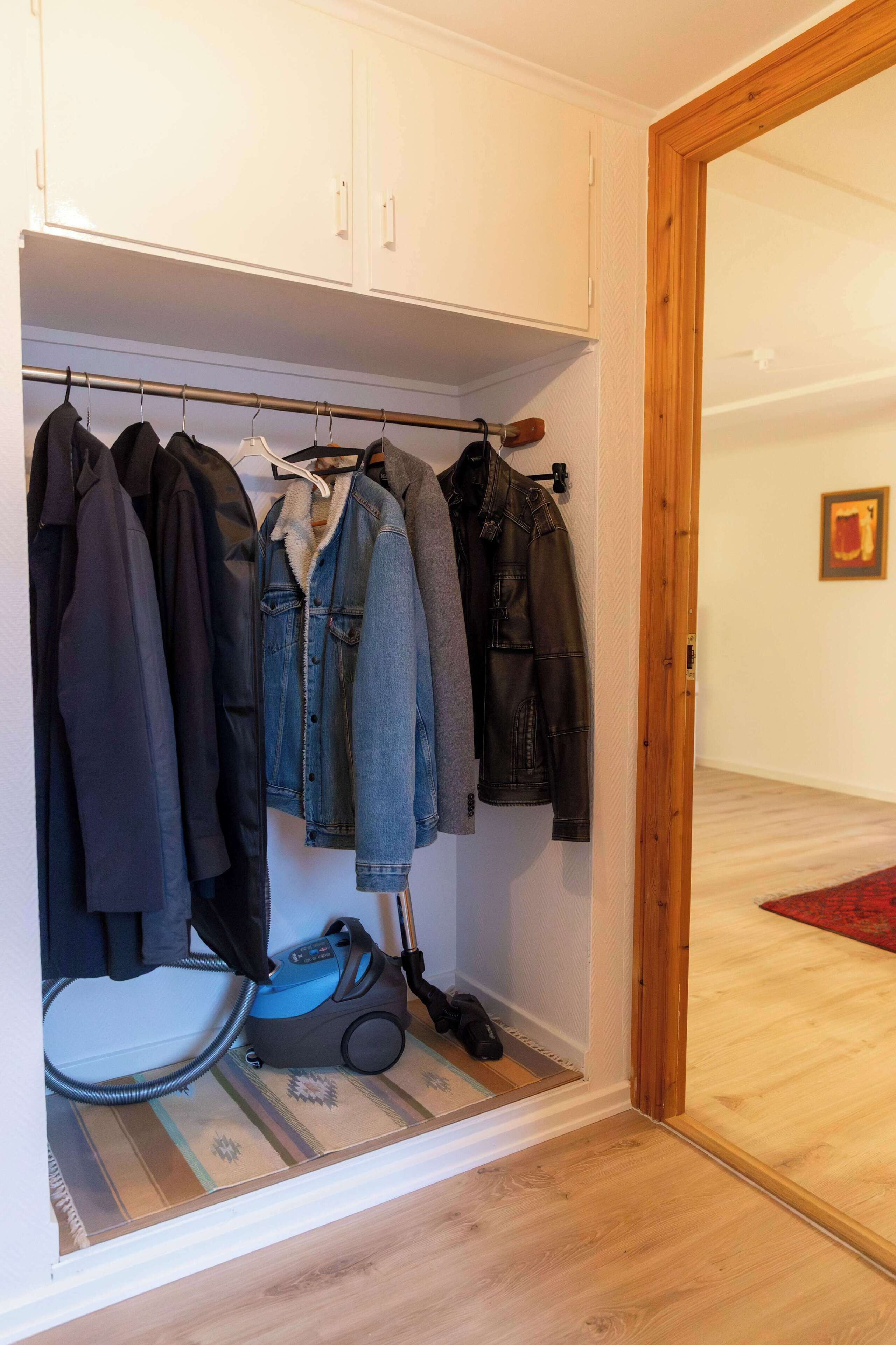 A walk-in closet with hanging clothes, a vacuum cleaner, and a patterned rug.
