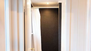 Ein schmales Badezimmer mit Toilette in Weiß, einer schwarzen Duschwand und einem weißen Duschvorhang.