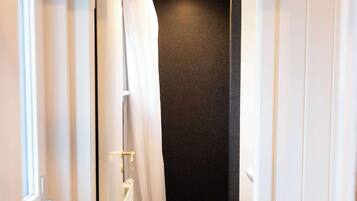A narrow bathroom with a white toilet, a black shower wall, and a white shower curtain.