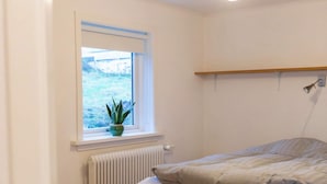 Ein Schlafzimmer mit einem Bett, einem Fenster mit Blick, einem Heizkörper und einer Pendelleuchte.