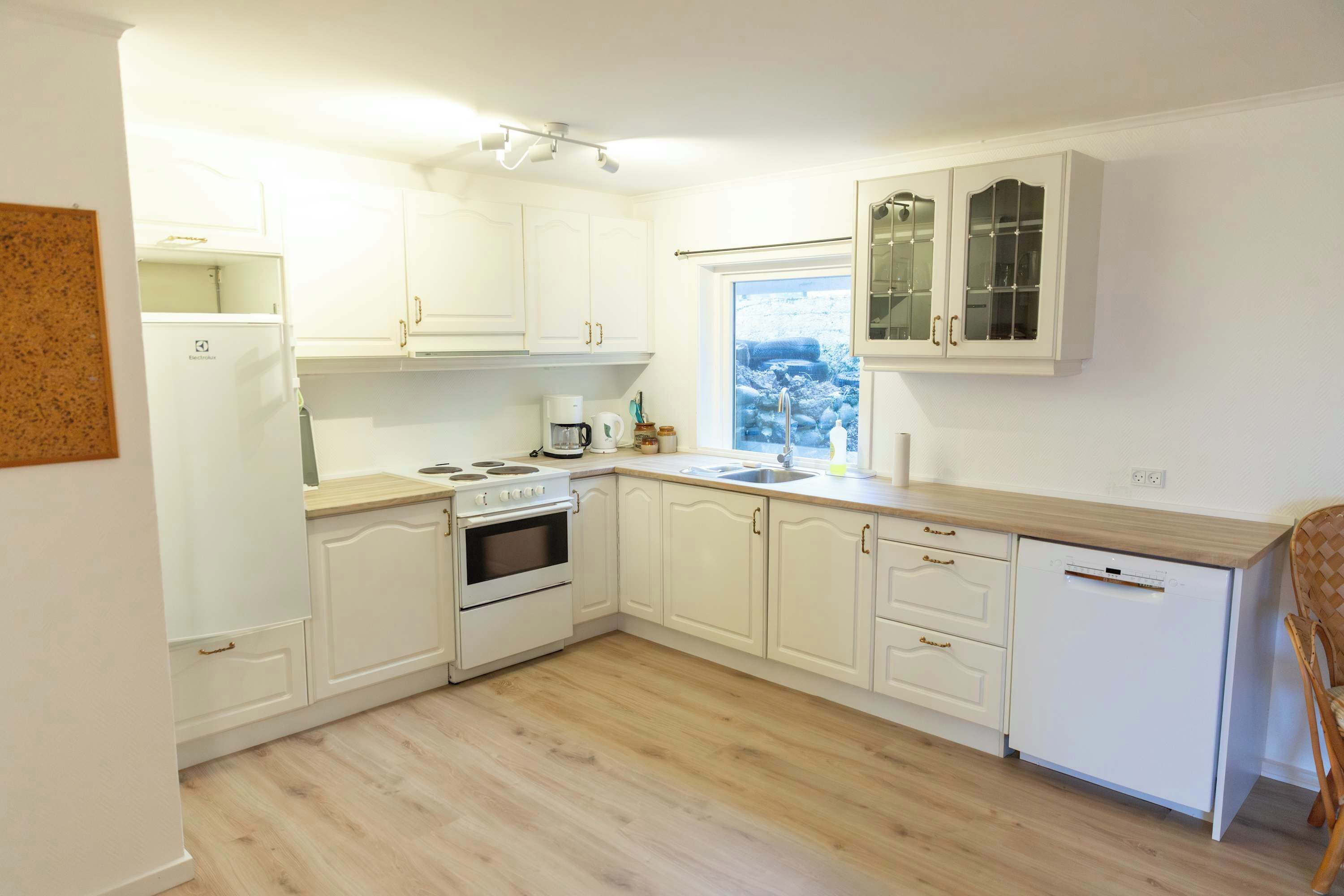 Una cocina con armarios blancos, estufa, lavaplatos y ventana con vistas.