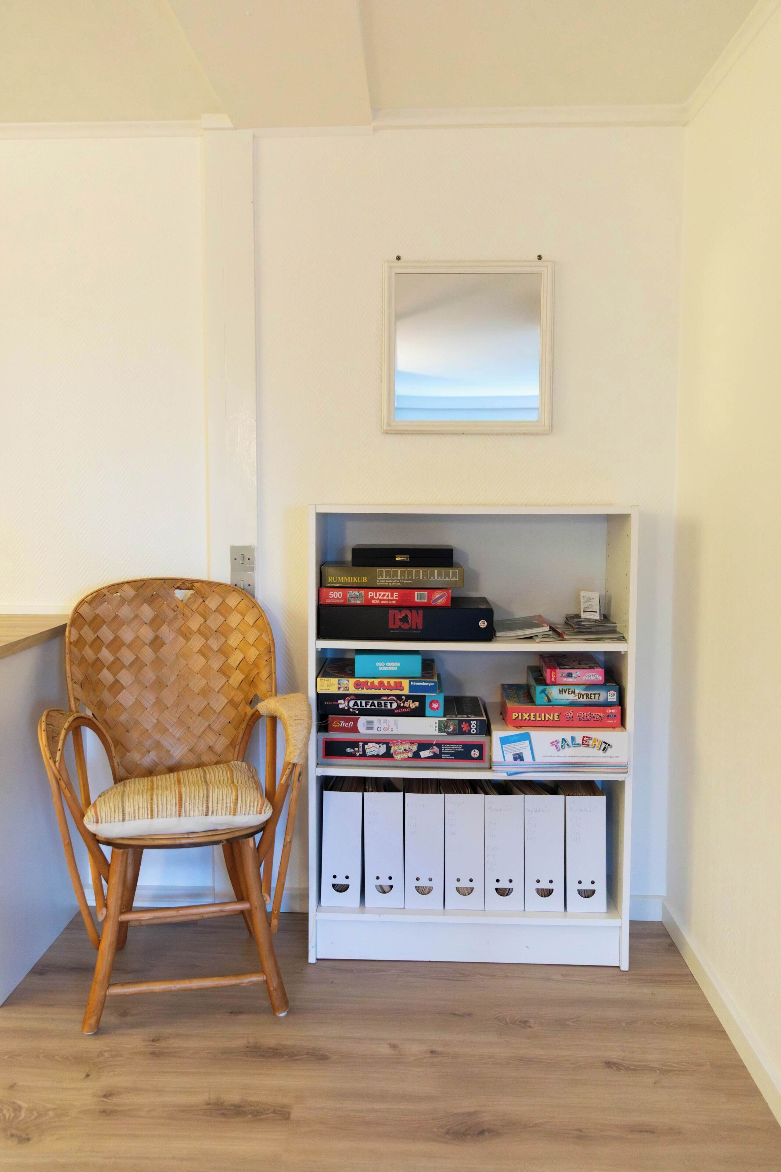 Ein Eckzimmer mit Holzstuhl, einem Bücherregal mit verschiedenen Gesellschaftsspielen und einem kleinen Fenster.