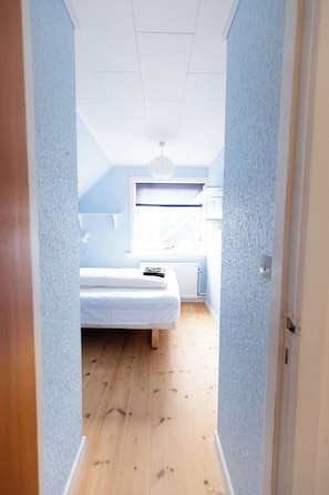 A narrow hallway leading to a bedroom with a bed, a window, and a ceiling light. - Spacious Villa in Torshavn City Centre - 10 Guests (Tórshavn)