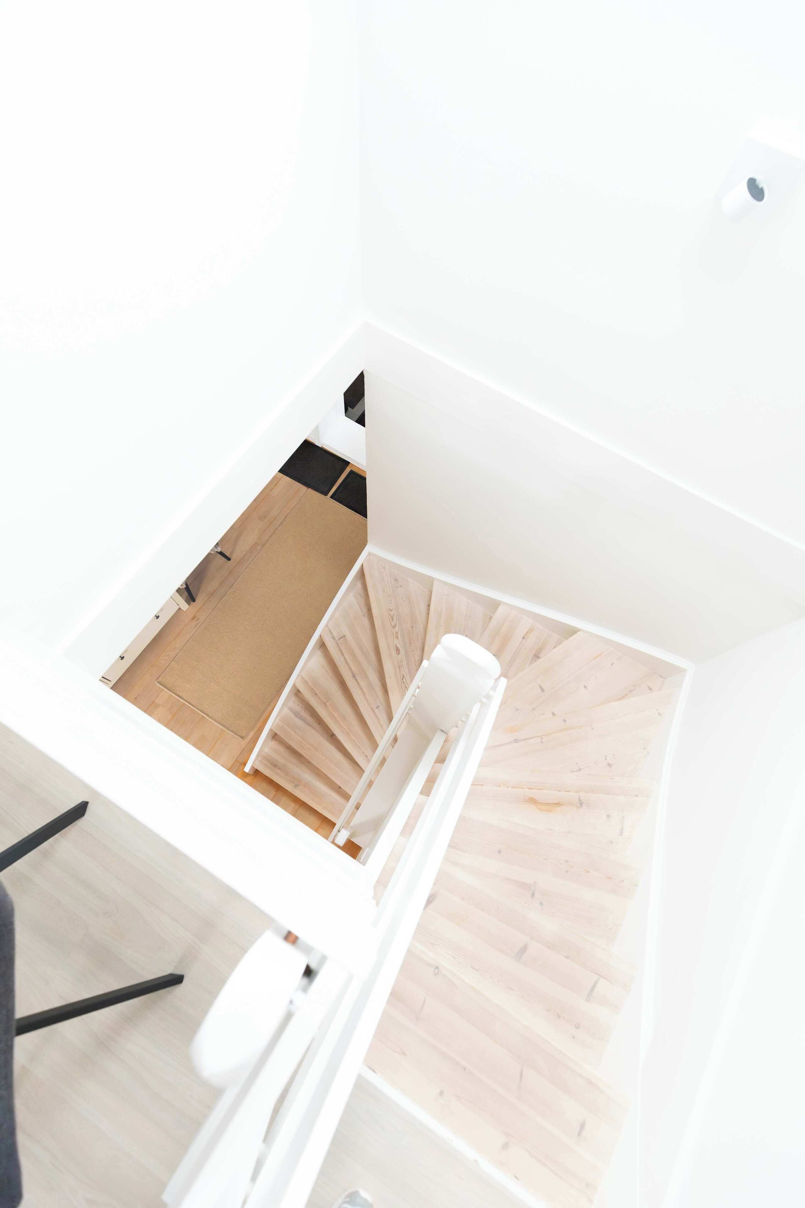 Vista aérea de una habitación moderna y minimalista con piso de madera, paredes blancas y una silla blanca.
