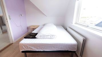 Habitació petita amb un llit individual, sostre inclinat, finestra amb vistes i un radiador.