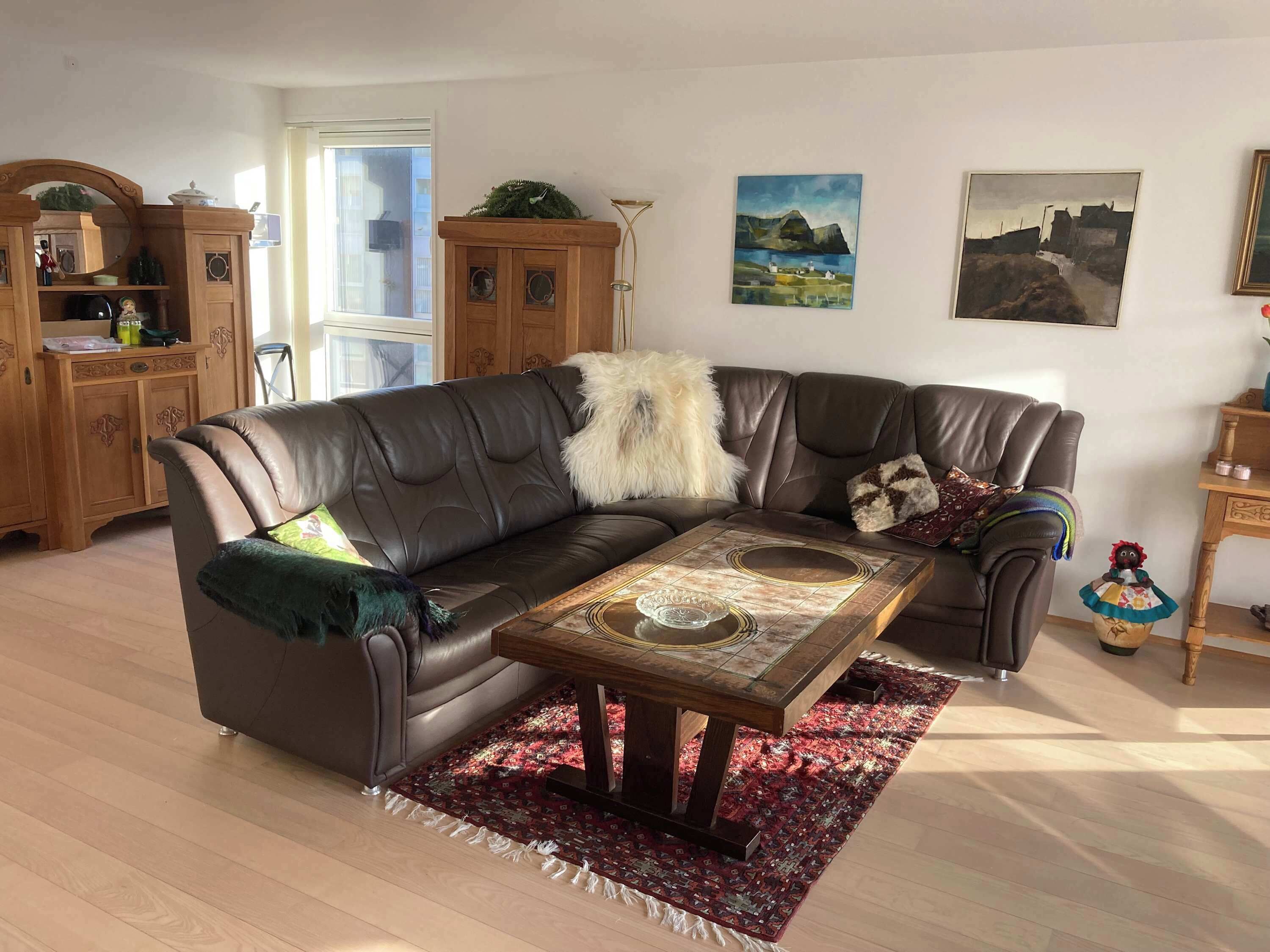 Una sala de estar con un sofá de cuero, una mesa de centro, un tapiz estampado y un mueble de madera.
