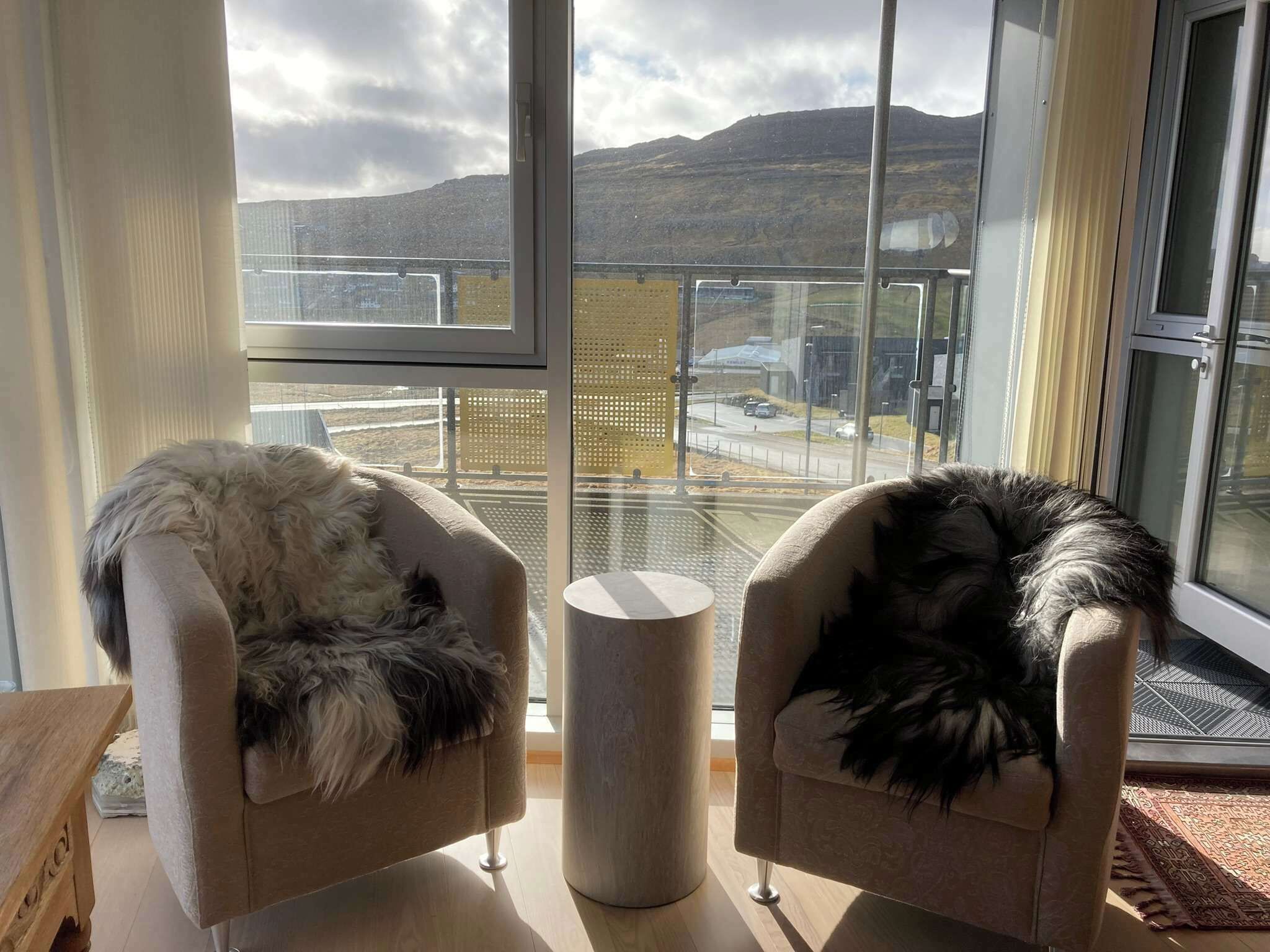 Zwei Sessel mit Felldecken, ausgerichtet auf ein großes Fenster mit Blick auf eine hügelige Landschaft.