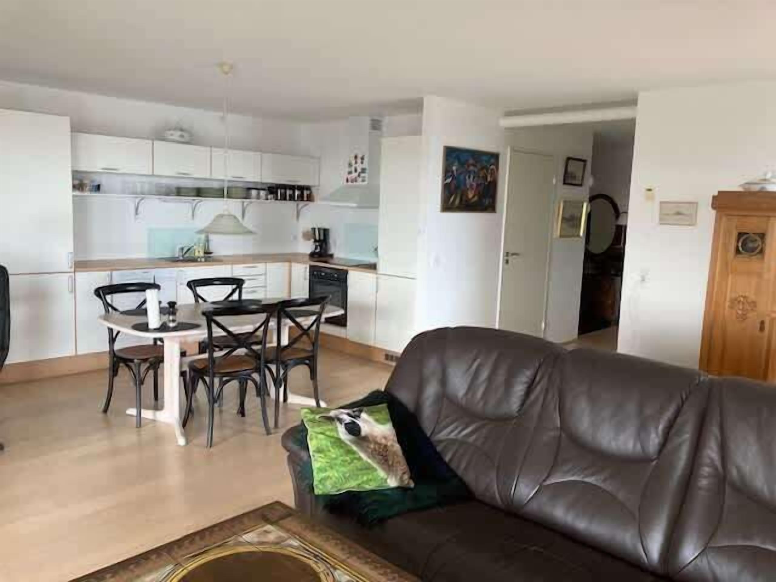 Een woonkamer met een leren bank, een eettafel met stoelen en een keuken op de achtergrond.