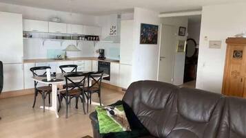 Een woonkamer met een leren bank, een eettafel met stoelen en een keuken op de achtergrond.