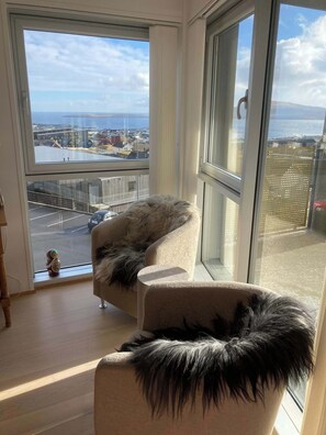 A room with a large window, a chair, and a view of a cityscape. - Panoramic Views of Torshavn and Nolsoy Fjord (Tórshavn)