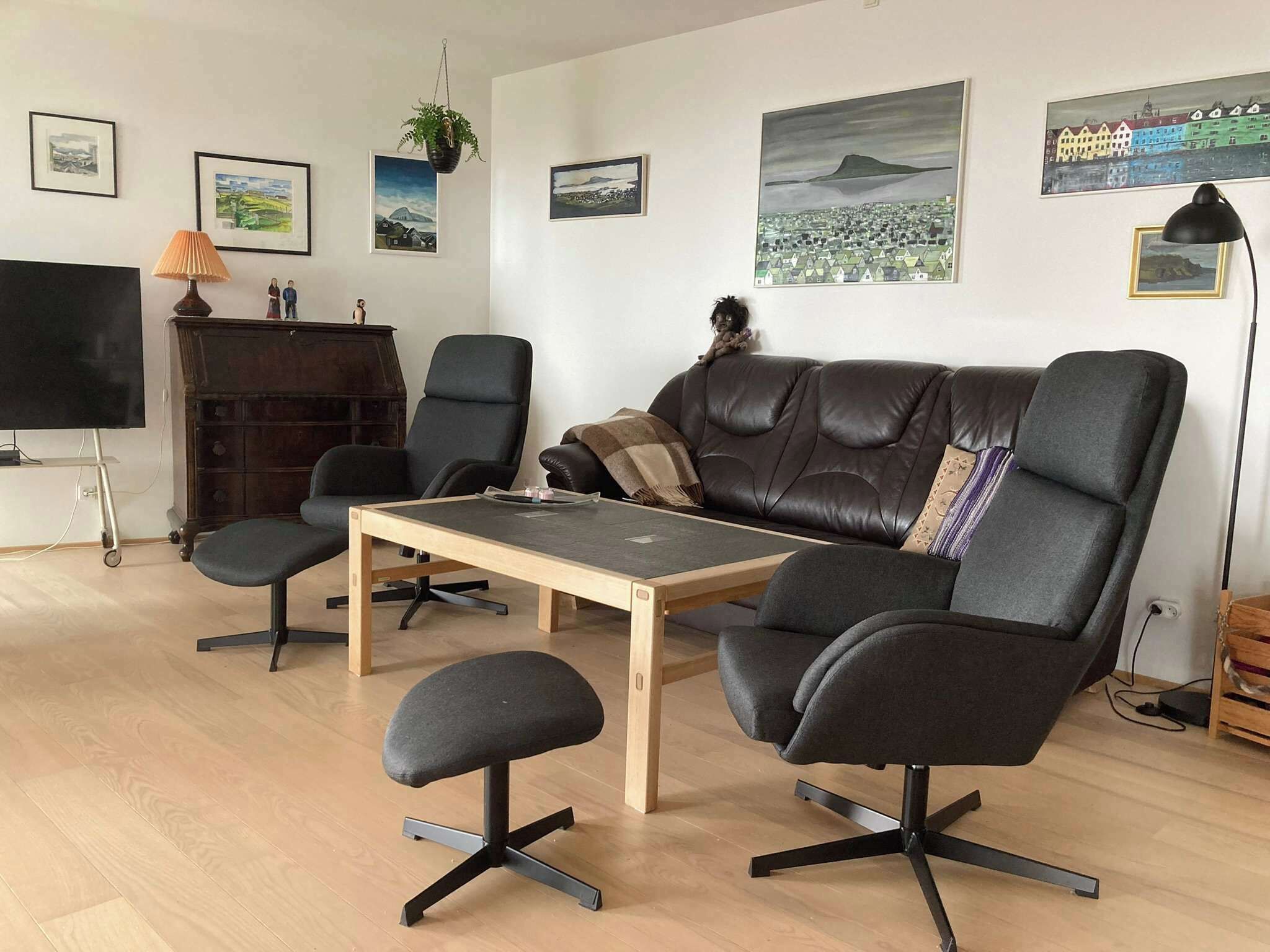 Ein modernes Wohnzimmer mit Ledersofa, zwei Sesseln, einem Couchtisch und einem Fernseher auf einem Lowboard.