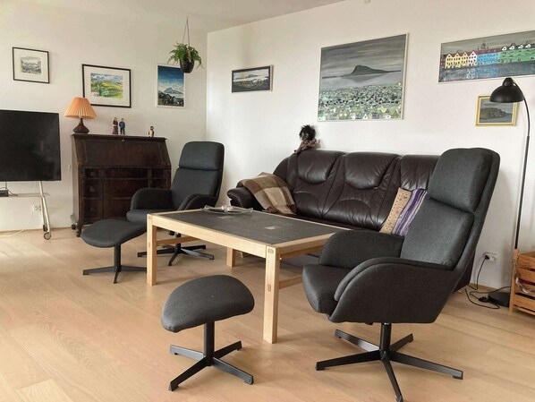 Una sala de estar moderna con un sofá de cuero, dos sillones, una mesa de centro y un televisor sobre un mueble.