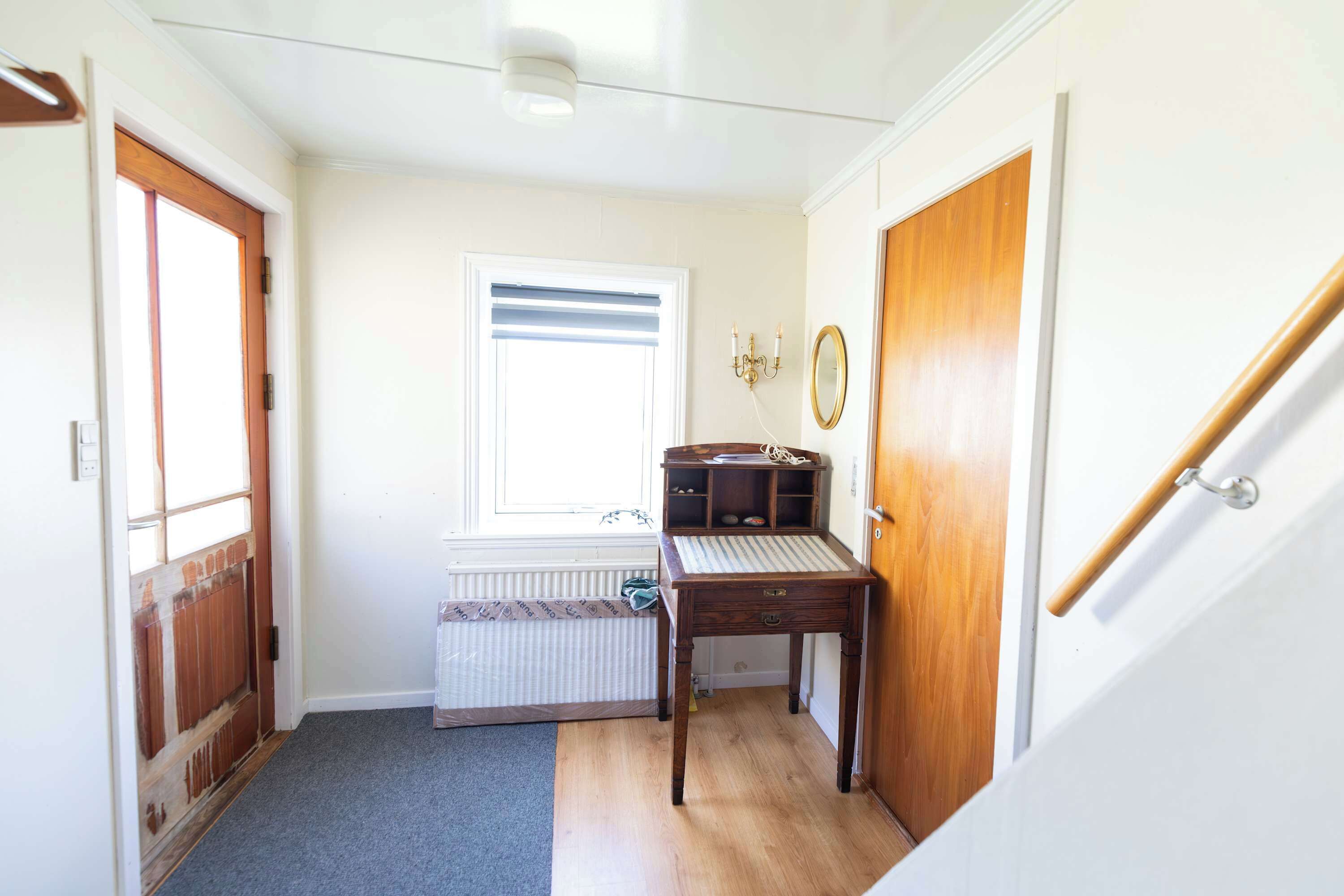 A hallway with a radiator, a wooden bench, a small table, and a door with a mirror.