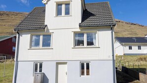 Ein zweistöckiges Haus mit Satteldach, einer Haustür und einem kleinen angebauten Schuppen.
