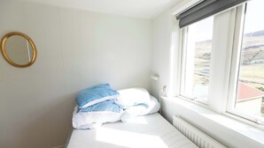 Ein Schlafzimmer mit Bett, Fenster mit Blick, Heizkörper und einem an der Wand befestigten Spiegel.