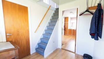 Una escalera que conduce a un segundo piso, una puerta de madera, un perchero con chaquetas y un par de zapatos en el suelo.
