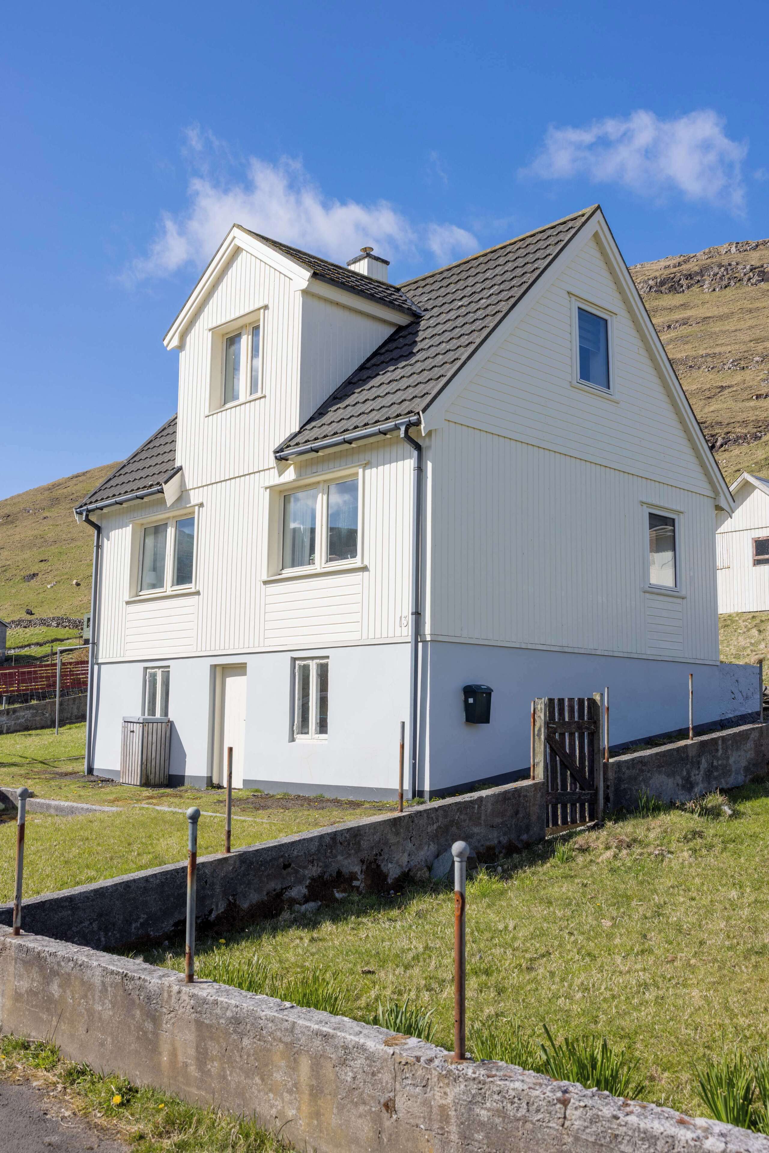 Une maison blanche à deux étages, dotée d’un toit à pignon, d’une porte d’entrée et d’un petit porche.
