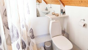 Ein kleines Badezimmer mit Holzboden, Toilette, Waschbecken und Duschbereich.