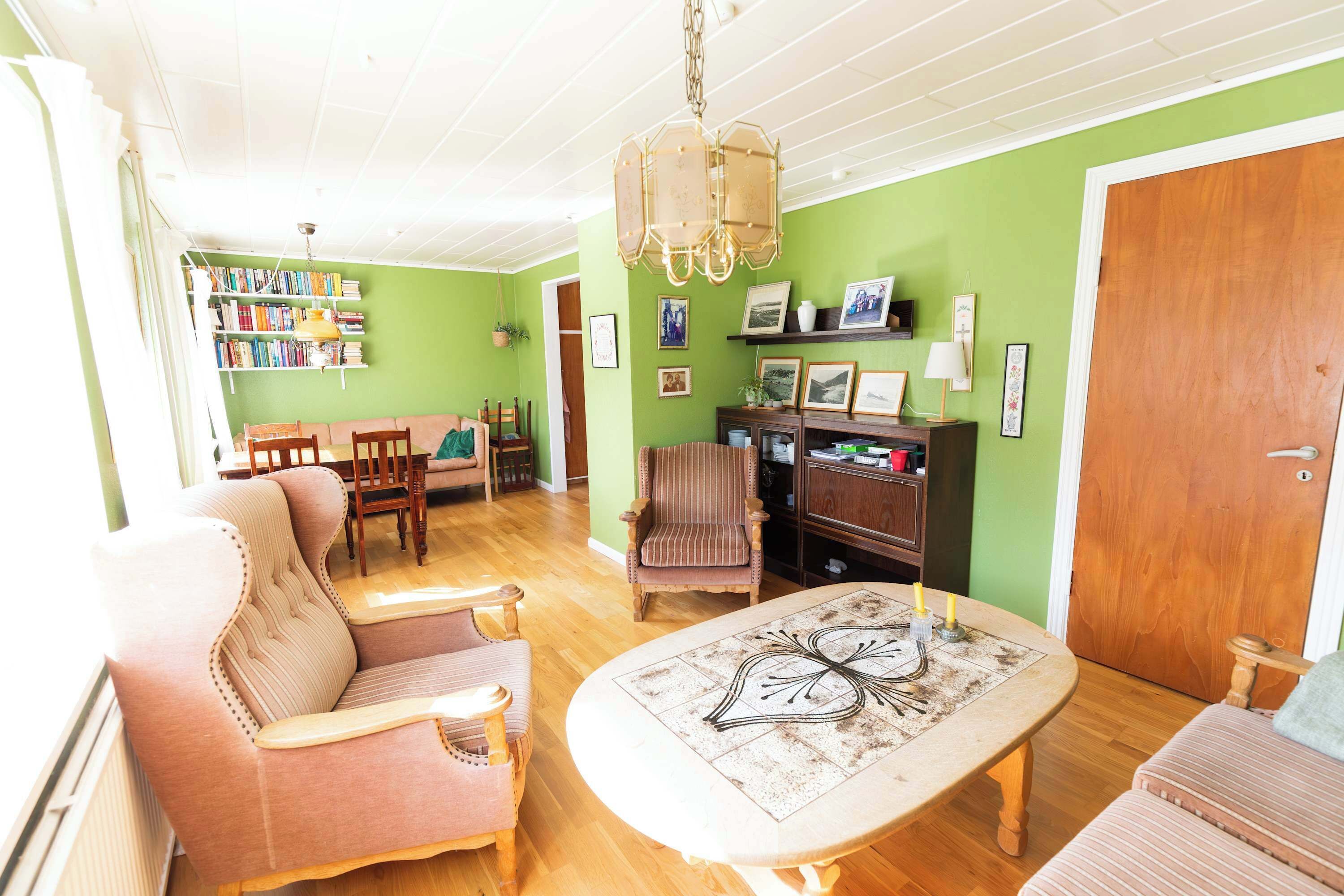Un salon avec un mur vert, des meubles en bois, un lustre et une bibliothèque.
